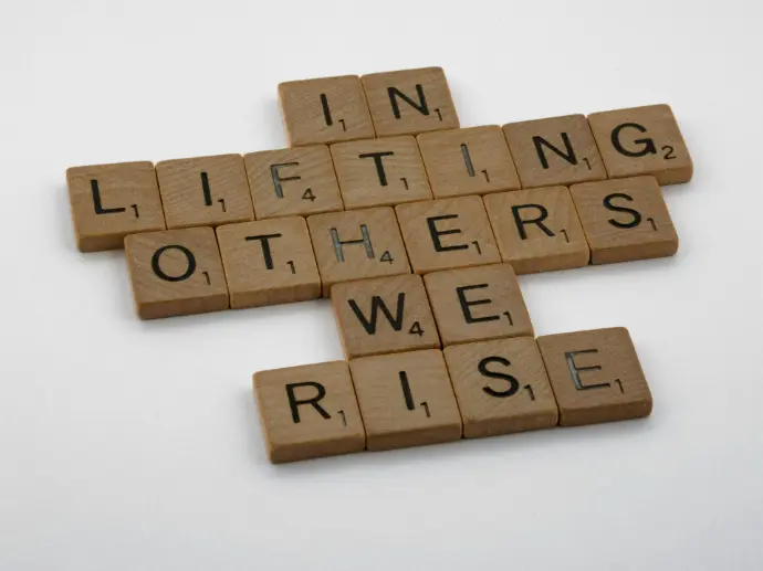 Wooden scrabble letters show the words 'in lifting others we rise'